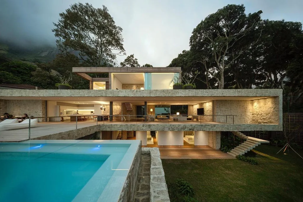 Modern multi-level luxury villa with an outdoor swimming pool, stone walls, and warm interior lighting.