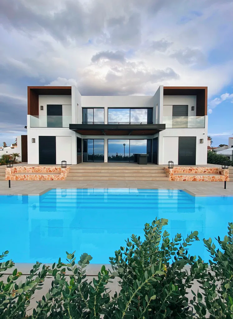 Modern multi-level luxury villa with a large outdoor swimming pool, white stucco exterior, wood accents, and glass balconies.
