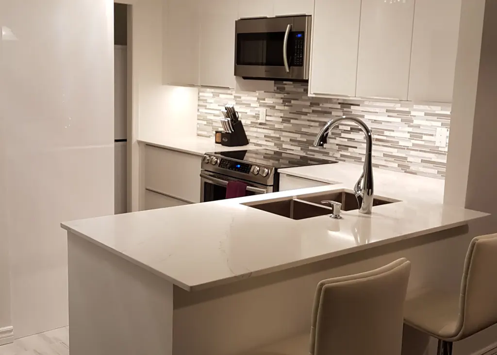 Modern white kitchen renovation featuring quartz countertops, a mosaic tile backsplash, and a breakfast bar with seating.