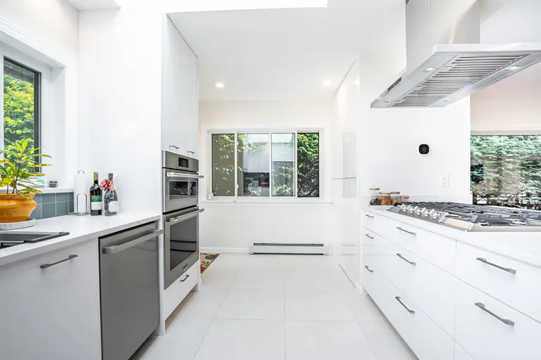 Modern white galley kitchen featuring flat-panel cabinets, white tile flooring, and stainless steel appliances.