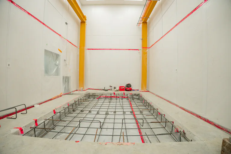 Structural steel rebar rebar grid installed in a excavated pit for concrete pouring inside an industrial building facility with yellow overhead cranes.