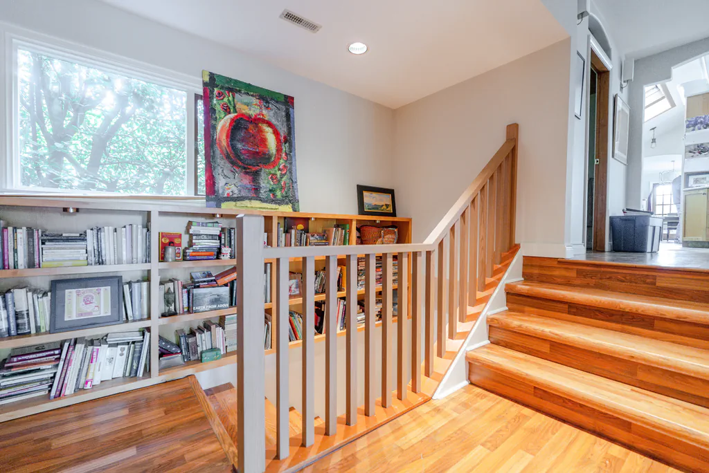 home interior featuring wooden stairs, a built-in bookshelf on the landing, and a colorful painting under a large window.