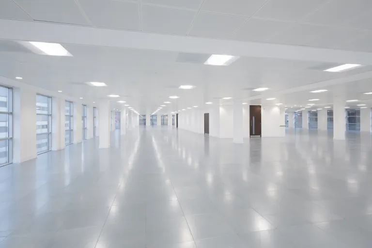 Empty, modern commercial office space with white pillars, bright recessed lighting, and glossy tiled floors.