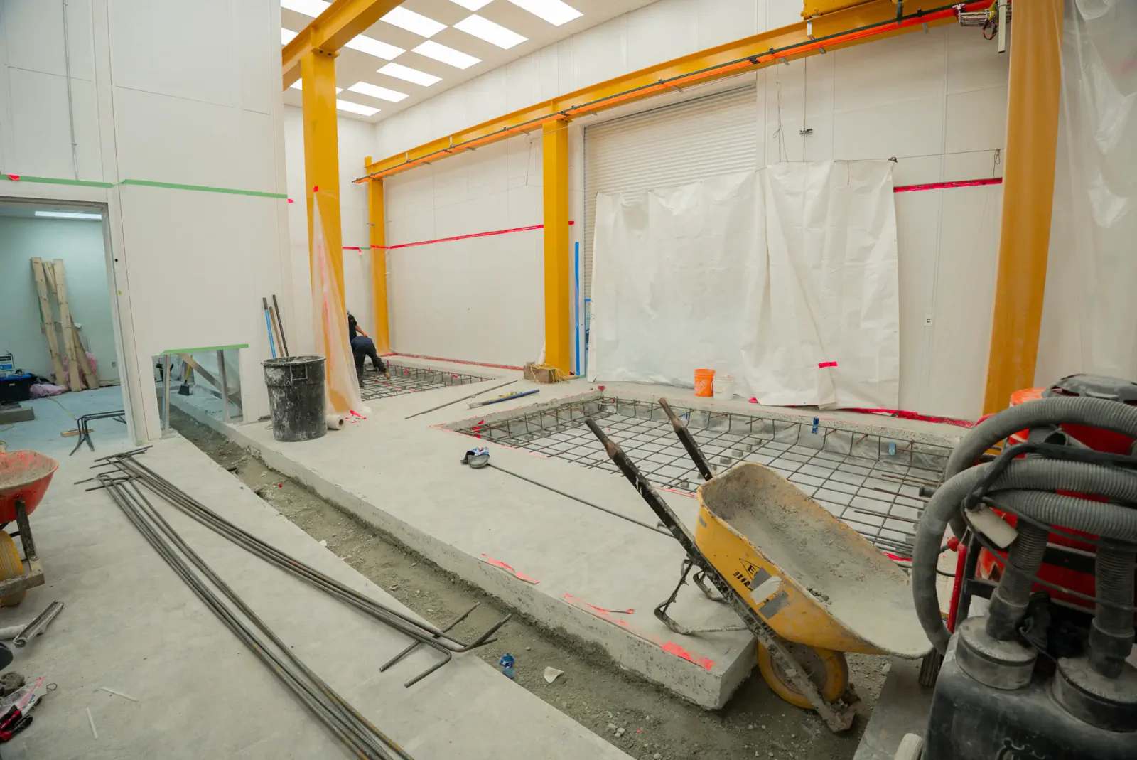 Freshly poured concrete slabs inside an industrial facility with yellow gantry cranes and protective wall sheeting.